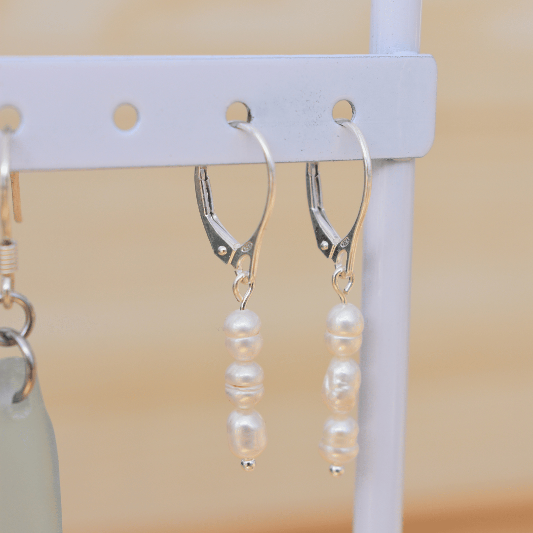 A pair of Salty Dreamers’ Pretty Pearly 925 silver leverback earrings, each with three freshwater pearls, displayed on a white holder against a light beige background.