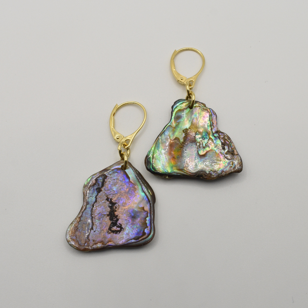 Salty Dreamers' Paua Shell Honu earrings feature irregular, iridescent New Zealand abalone shells on gold lever-back hooks, showcased on a plain light gray background.