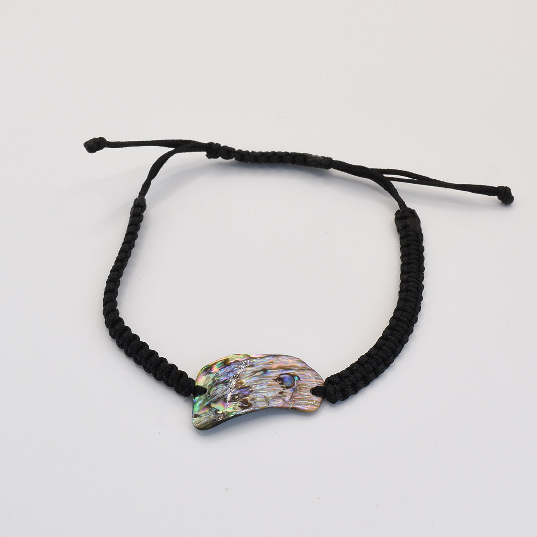 The Salty Dreamers Bracelet | Paua Shell Uru is a handmade black braided bracelet with an iridescent, claw-shaped New Zealand abalone shell centerpiece, shown on a plain white background.