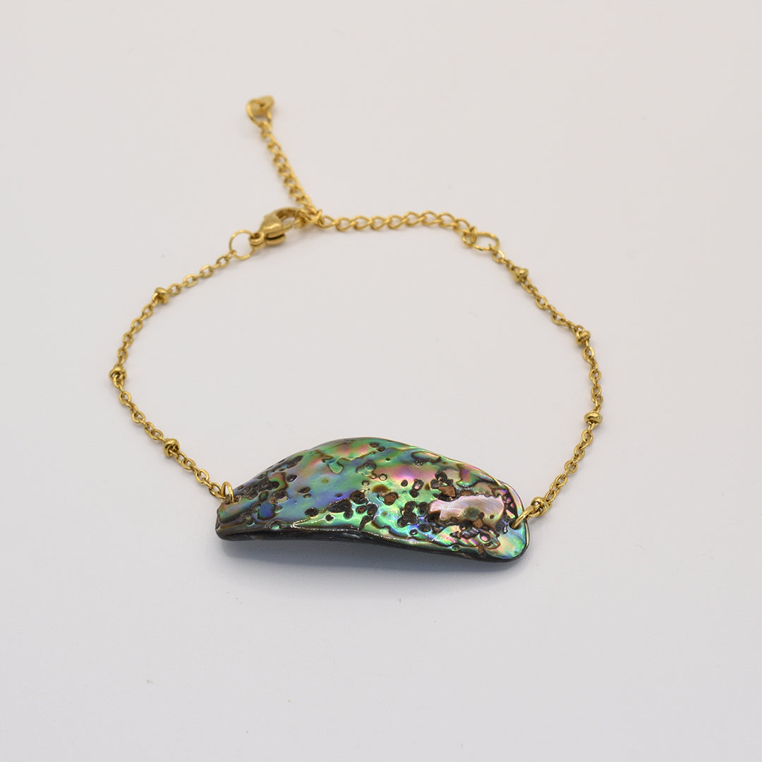 The Bracelet | Paua Shell Mahaki by Salty Dreamers features a gold chain and curved iridescent abalone centerpiece with green, blue, and pink hues—an elegant handmade New Zealand jewelry piece shown on white.
