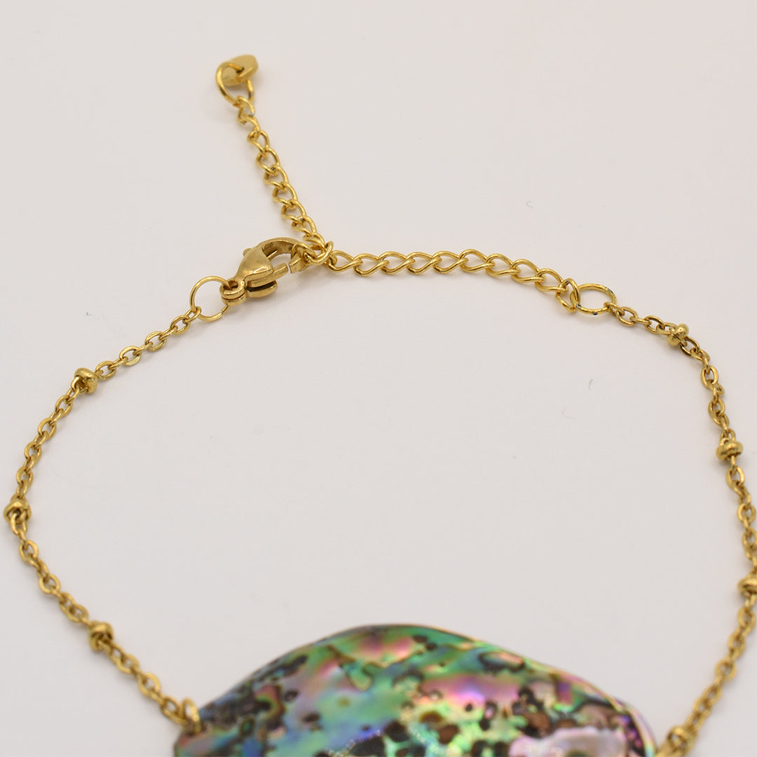 A close-up of the Salty Dreamers Bracelet | Paua Shell Mahaki shows its iridescent paua shell centerpiece on a gold chain with lobster clasp and adjustable links, highlighted against a white background. Elegant handmade New Zealand jewelry.