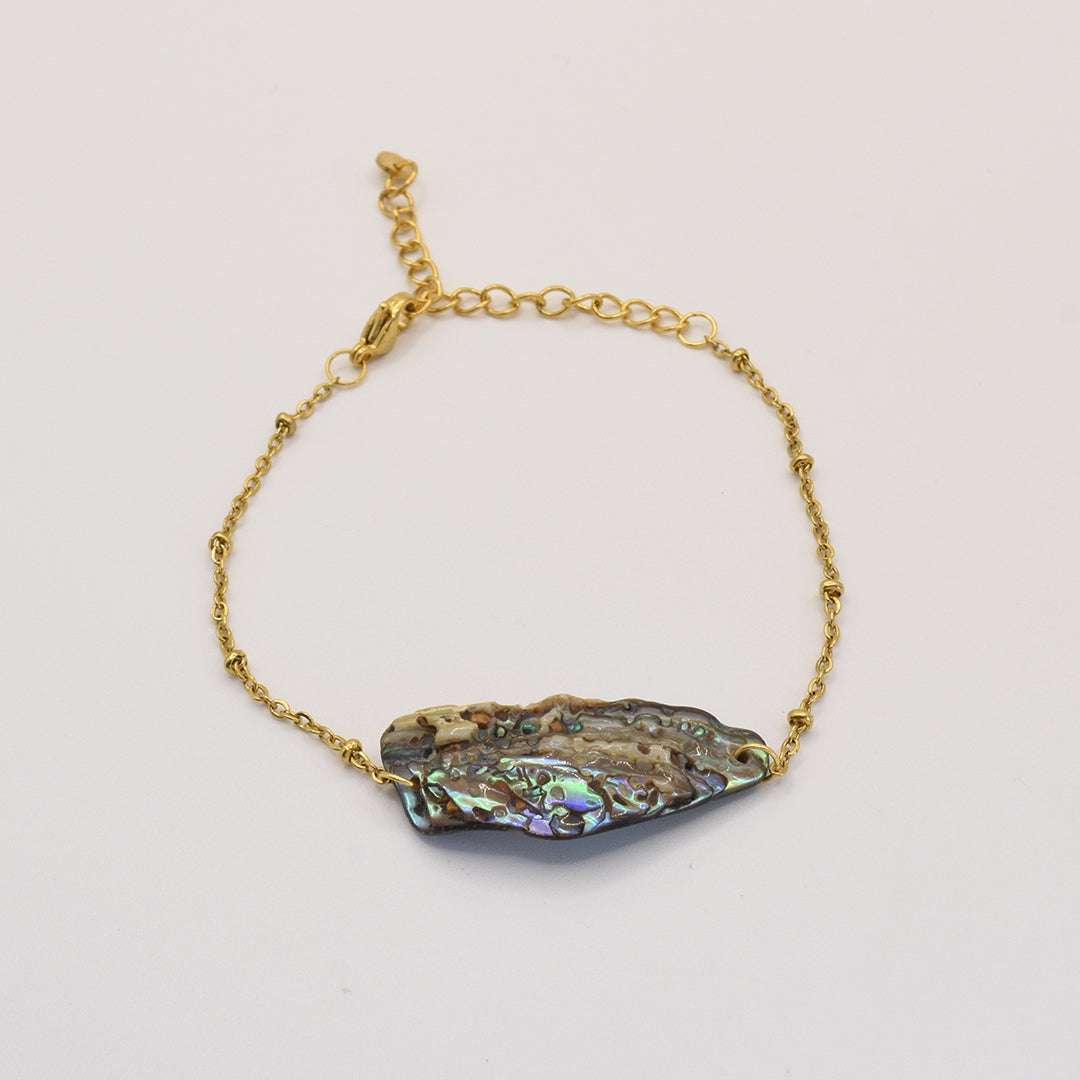 The Bracelet | Paua Shell Takaro by Salty Dreamers is a handmade gold chain bracelet featuring an irregular, multicolored pāua shell centerpiece, shown against a plain white background.