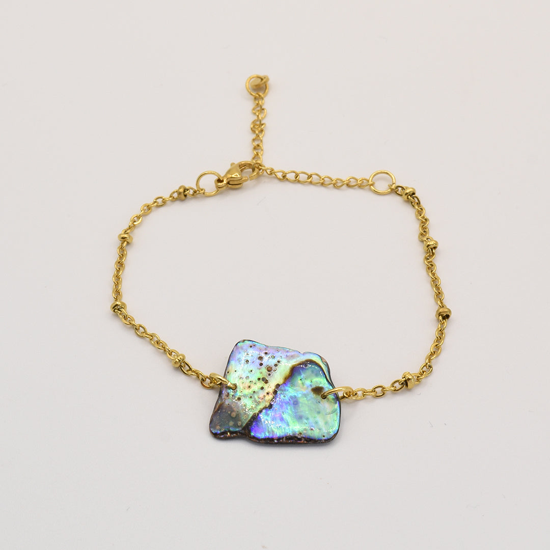 The Salty Dreamers Bracelet | Paua Shell Whenua features a delicate gold chain with an iridescent, uniquely shaped pāua shell centerpiece, highlighting abalone jewelry artistry against a plain light background.