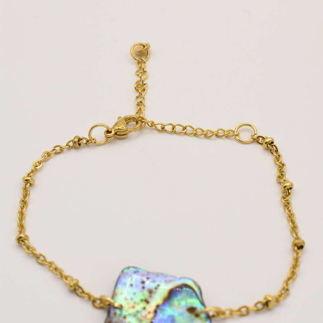 The Salty Dreamers Bracelet | Paua Shell Whenua features a gold chain with an iridescent pāua shell centerpiece, shown on a light background. An open clasp and small extender offer adjustable sizing—a stunning piece of New Zealand jewelry.