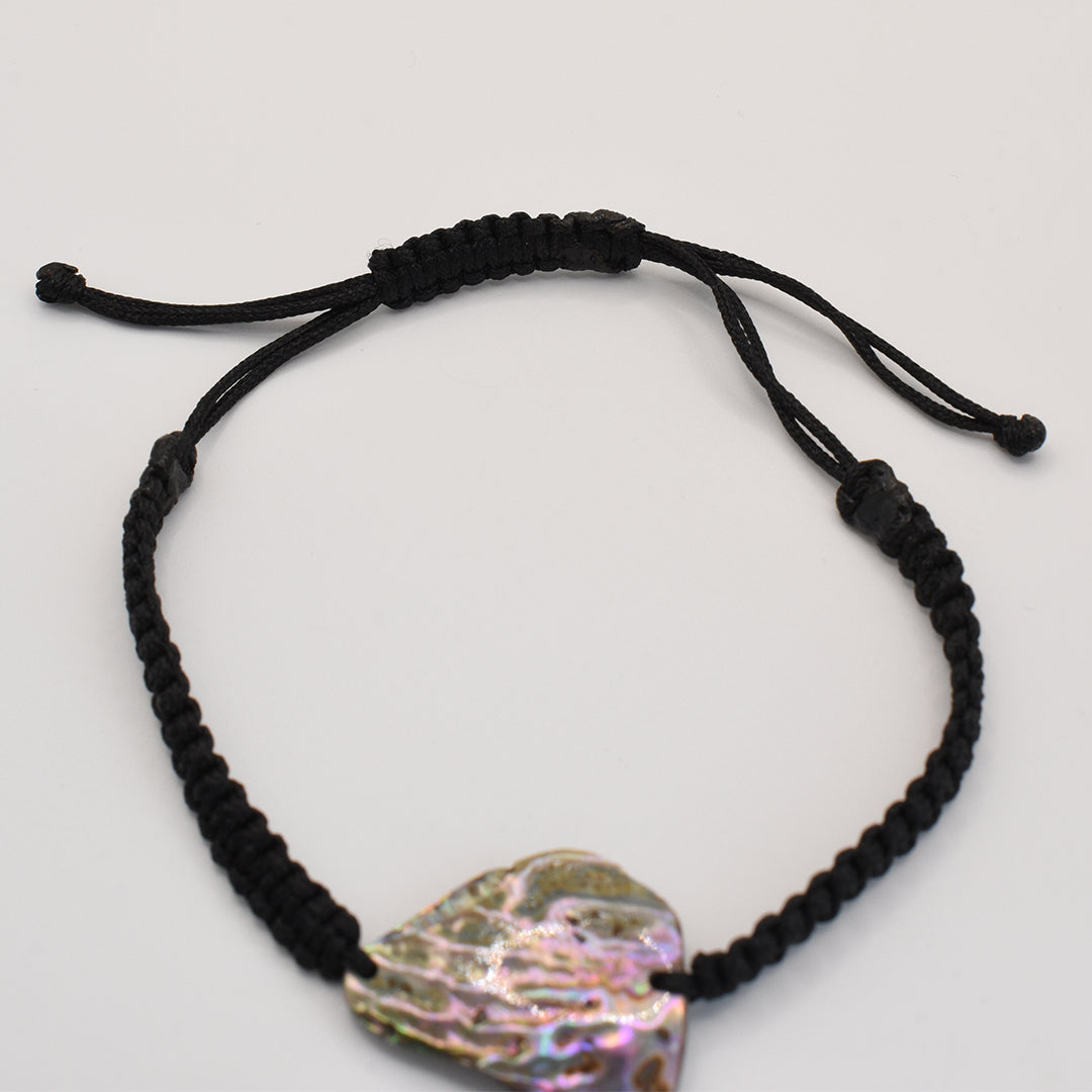 The Salty Dreamers Bracelet | Paua Shell Kaha features a handmade, black braided cord with an adjustable knot and an iridescent paua shell centerpiece, reflecting the elegant beauty of New Zealand jewelry. Shown on a plain white background.