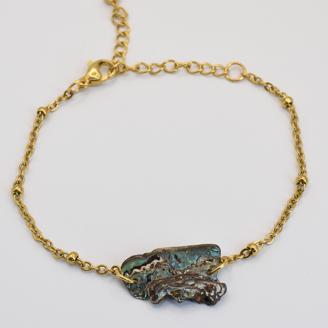 The Bracelet | Paua Shell Marie by Salty Dreamers features a delicate gold chain and an irregular, textured pāua shell centerpiece in blue-green tones—a striking piece of New Zealand jewelry, shown on a plain white background.