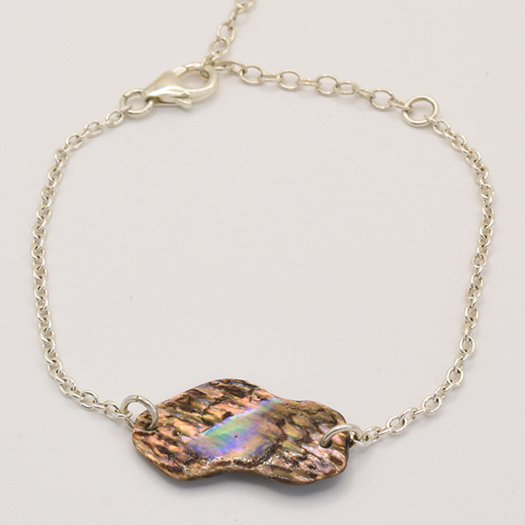 The Salty Dreamers Bracelet | Paua Shell One showcases an iridescent, handmade irregular pāua shell centerpiece set in delicate 925 silver with a lobster clasp, styled on a plain light background.