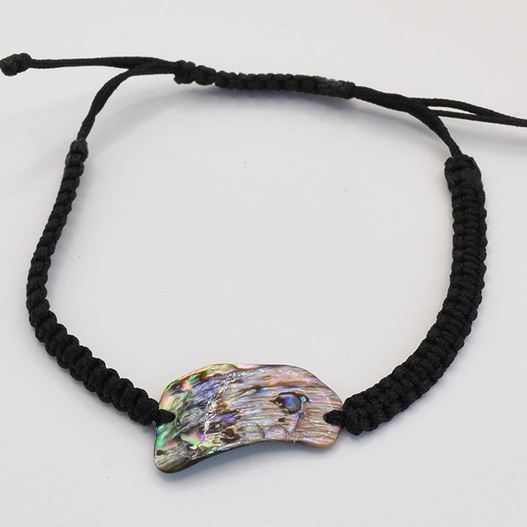 The Salty Dreamers Bracelet | Paua Shell Uru features a handmade black braided cord and a curved New Zealand abalone shell centerpiece with natural iridescent patterns, shown on a plain white background.