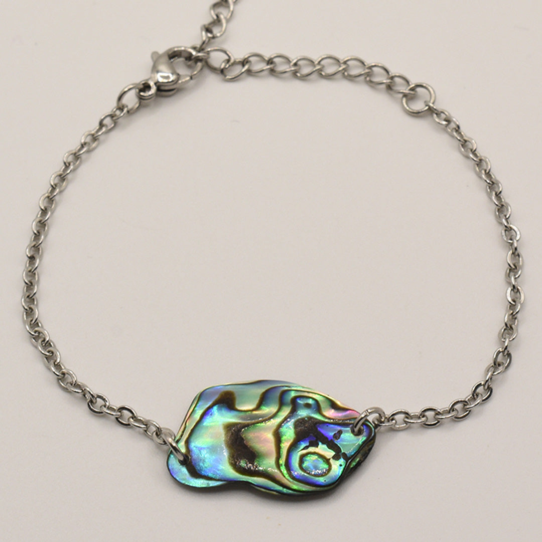 The Salty Dreamers Bracelet | Paua Shell Tumanako features a handcrafted silver chain, an iridescent abstract pāua shell centerpiece, and a lobster clasp, displayed on a plain light background. Inspired by New Zealand craftsmanship.