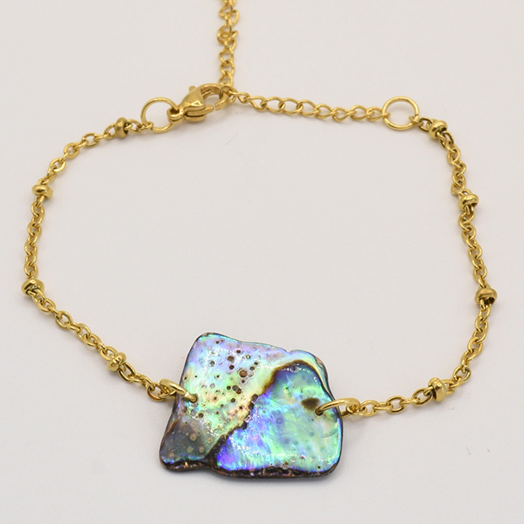 The Salty Dreamers Bracelet | Paua Shell Whenua features an iridescent, irregularly shaped pāua shell on a gold chain with lobster clasp—an elegant abalone jewelry piece inspired by New Zealand traditions.