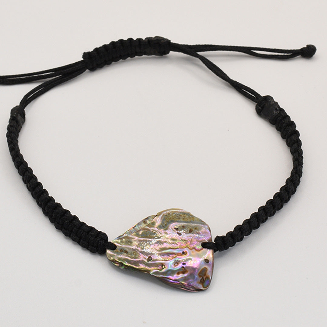 The Salty Dreamers Bracelet | Paua Shell Kaha is a handmade black braided cord bracelet with an iridescent, irregular pāua shell centerpiece, shown on a plain white background.
