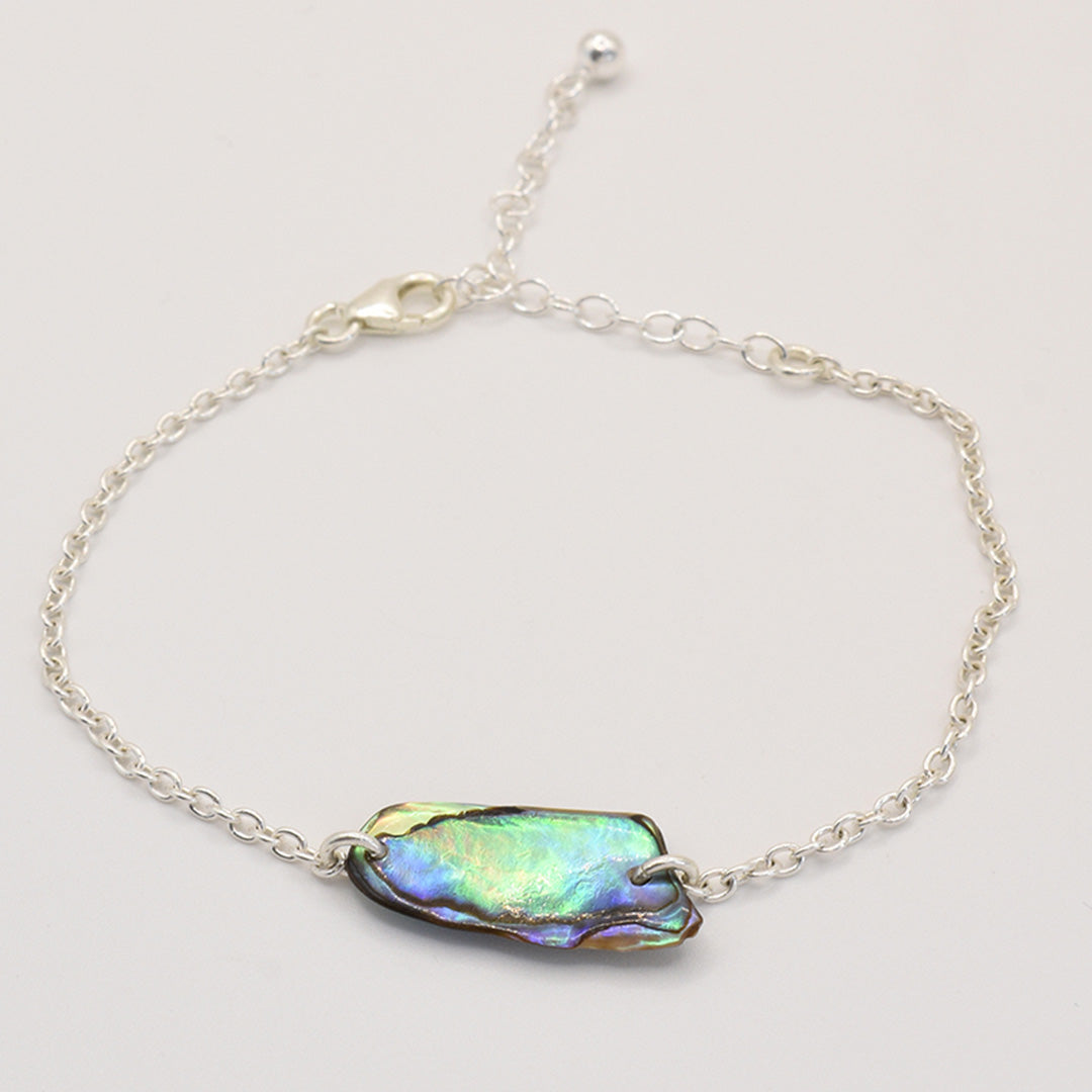 The Bracelet | Paua Shell Toi by Salty Dreamers features a delicate handmade silver chain with an iridescent New Zealand abalone shell centerpiece, adjustable lobster clasp, and is showcased on a plain white background.