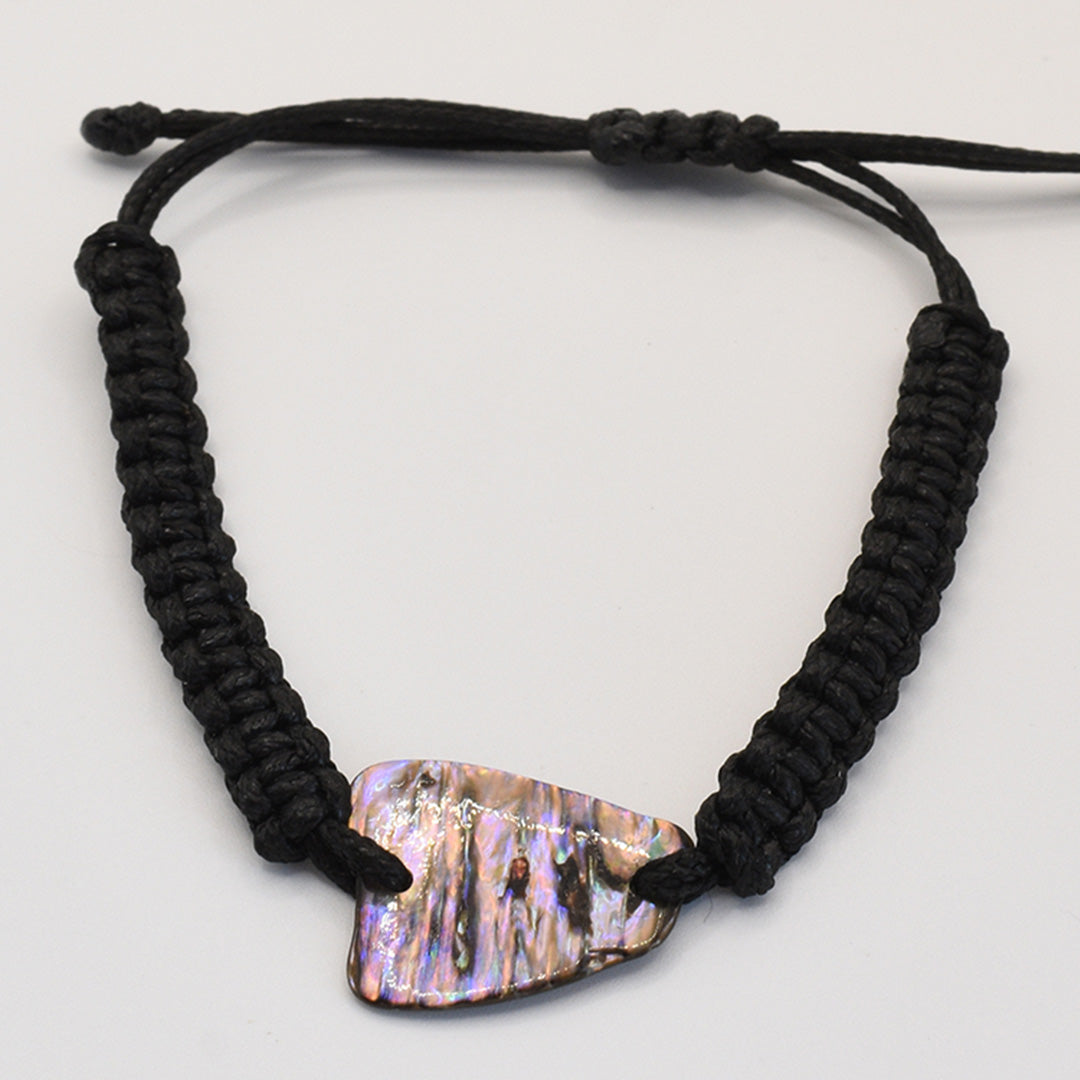 The Salty Dreamers Bracelet | Paua Shell Toa is a black, handmade macrame-style bracelet with a polished, iridescent New Zealand abalone shell centerpiece, displayed on a plain white background.