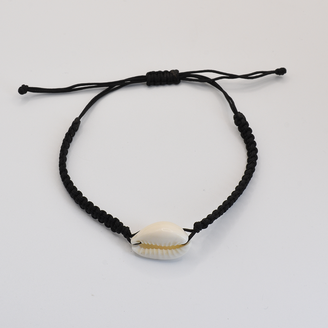 The Salty Dreamers Macramazing Cowrie Black bracelet features a handmade black braided band with a single white cowrie shell at the center, shown on a plain white background.