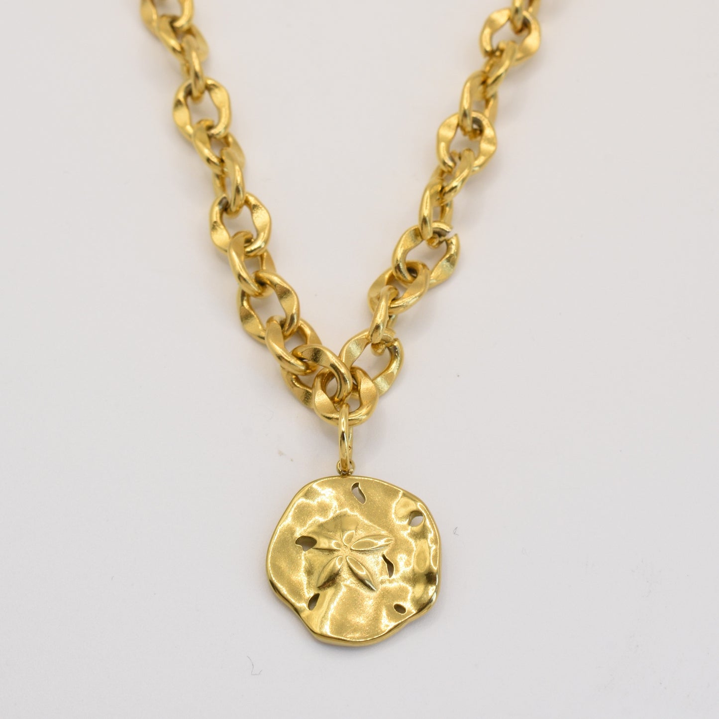 The Salty Dreamers Necklace | Ocean Dollar Gold features large gold links and a round, hammered pendant with a subtle sand dollar design—an ocean-inspired, handmade piece of jewelry shown on a plain white background.