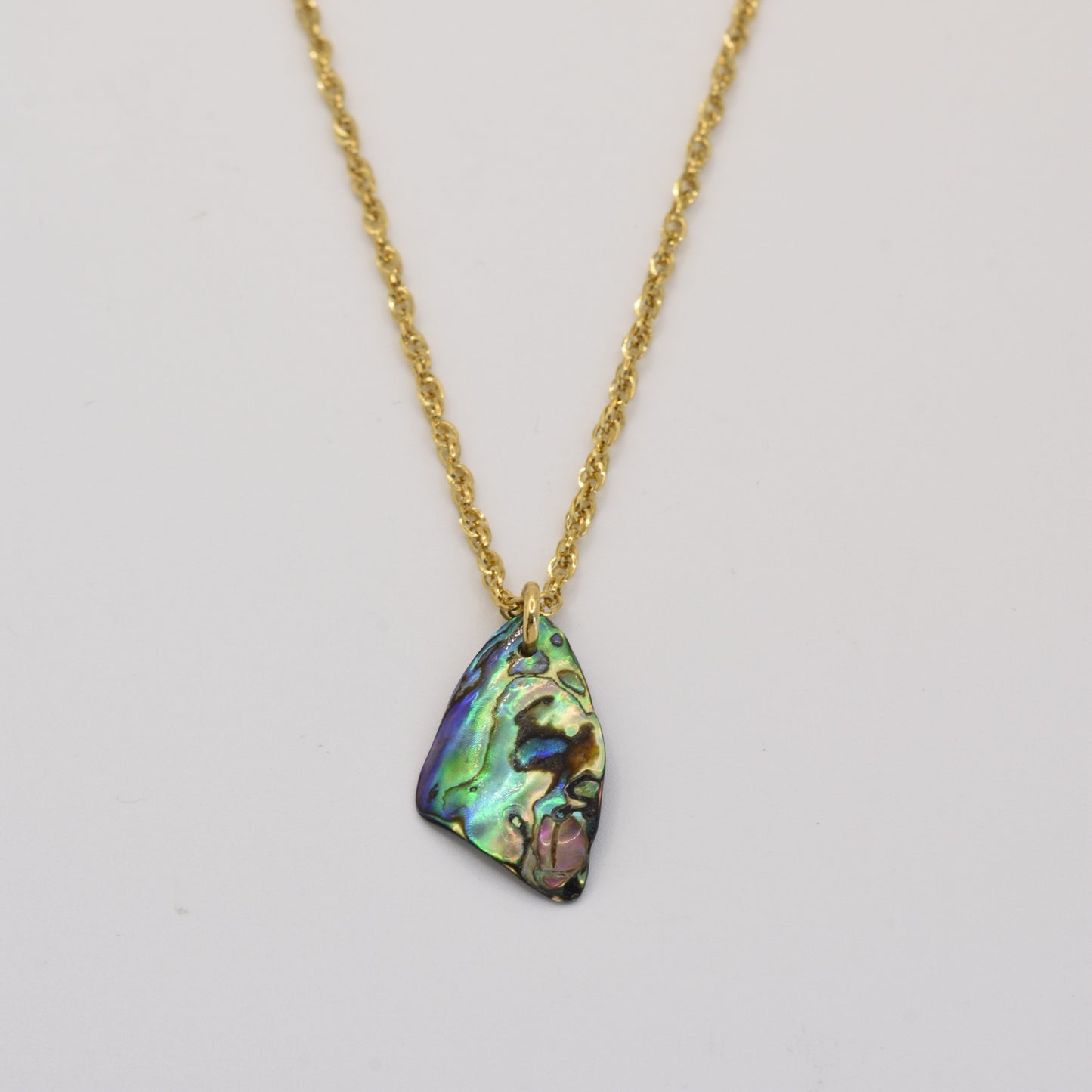 The Salty Dreamers Necklace | Paua Shell Kopiko features a golden stainless steel chain and an iridescent paua shell pendant with green, blue, and purple hues, shown on a plain white background.