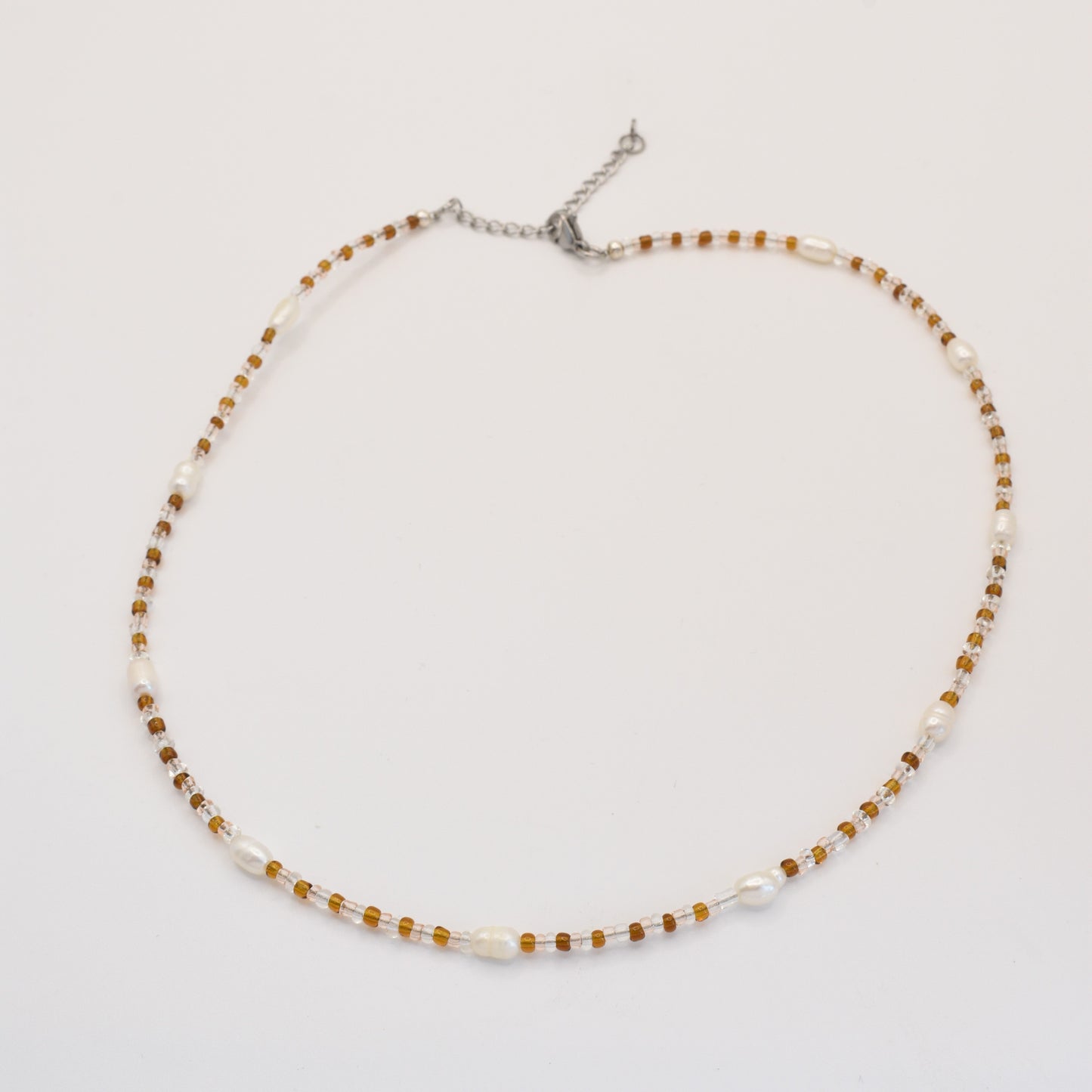 The Caramel Whispers necklace by Salty Dreamers features alternating small brown beads and white freshwater pearls on a silver adjustable chain, elegantly displayed on a plain white background.