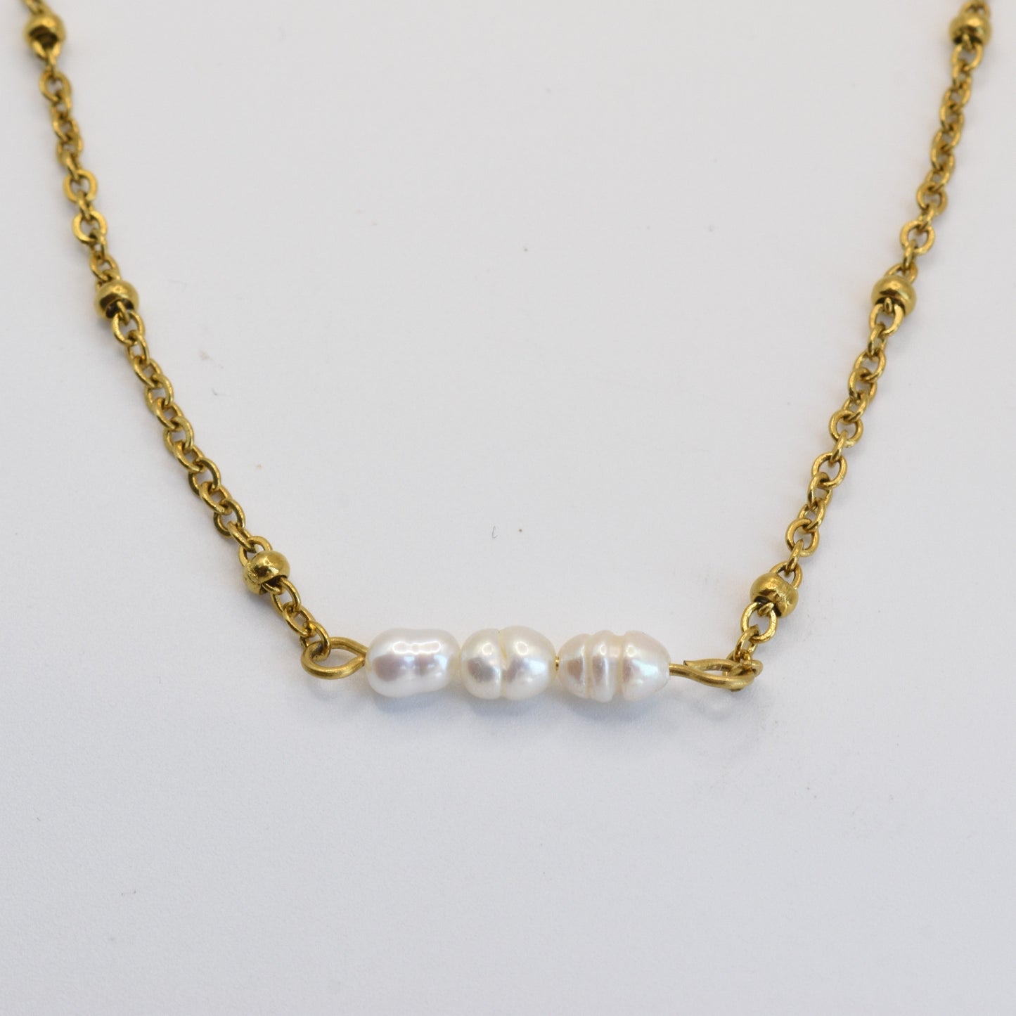 The Pretty Pearly Gold Necklace by Salty Dreamers features a delicate gold chain with three small, irregular freshwater pearls in a row, showcased on a simple white background.