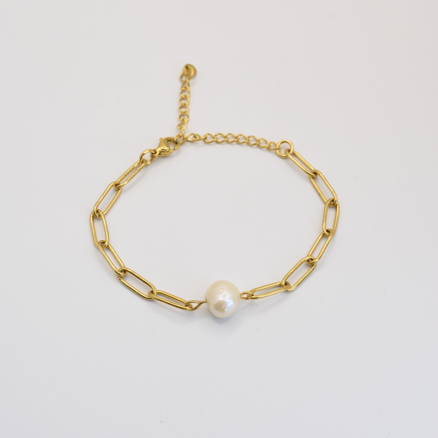 The Paperclip Cutie Gold bracelet by Salty Dreamers features elongated gold links, a single freshwater pearl centerpiece, and an adjustable clasp. This handmade piece is displayed on a plain white background.