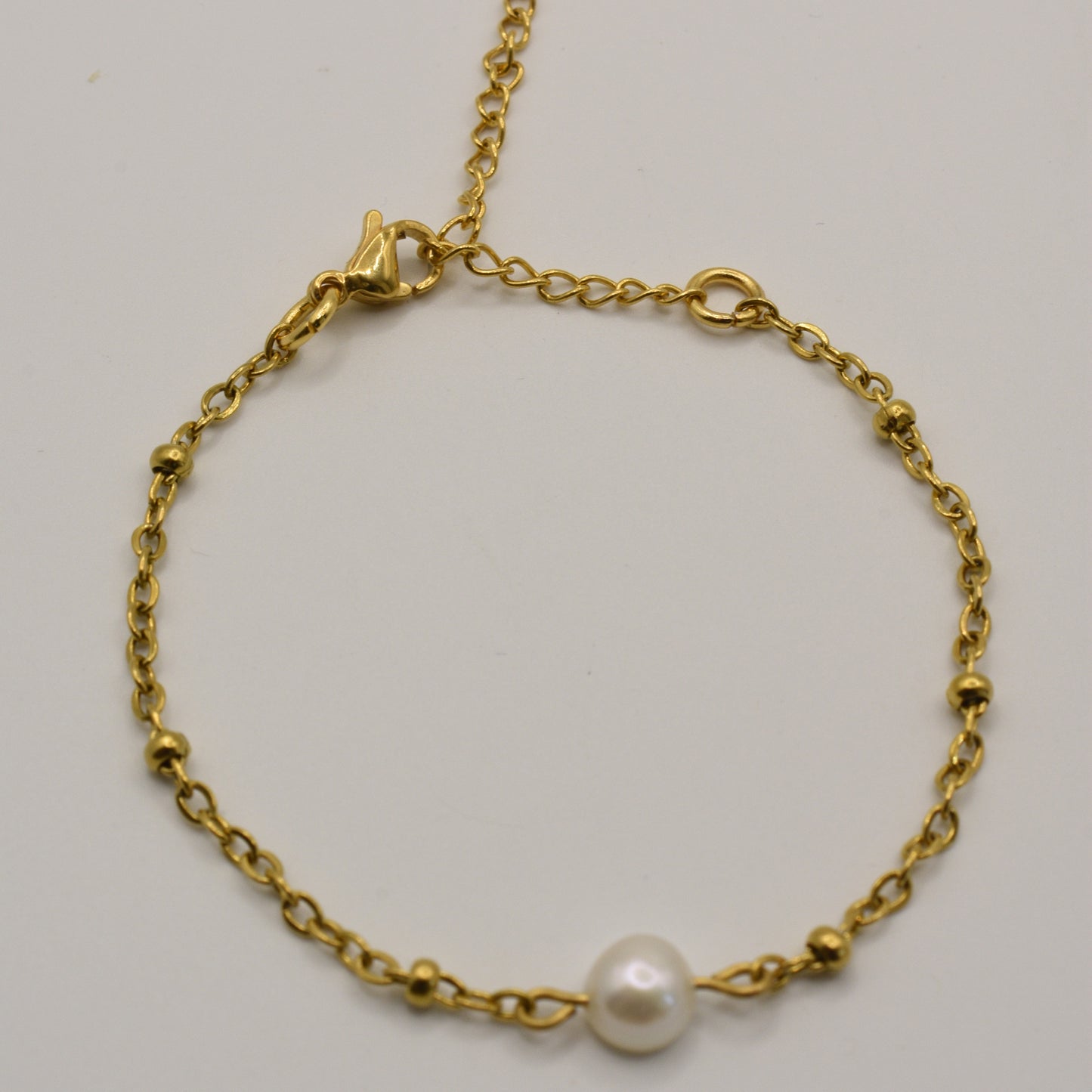 The Salty Dreamers Bracelet | Cutie Pearly Gold is a delicate handmade piece featuring a single white pearl centerpiece, gold bead accents, and a lobster clasp, displayed on a plain white background.