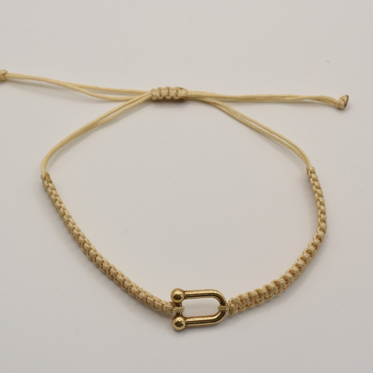 The Salty Dreamers Bracelet | Sailors Love Beige is a handmade macramé bracelet in beige with a small gold U-shaped clasp, inspired by classic sailor shackle bracelets and displayed on a plain white background.