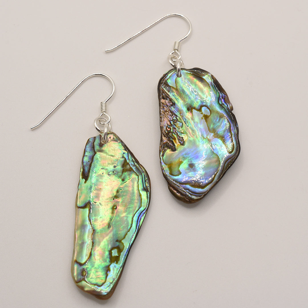 Salty Dreamers’ Earrings | Paua Shell Raumati: Handmade abalone earrings with irregular iridescent green, blue, and purple pāua shell pendants on silver hooks. A unique piece of New Zealand jewelry set against a plain white background.
