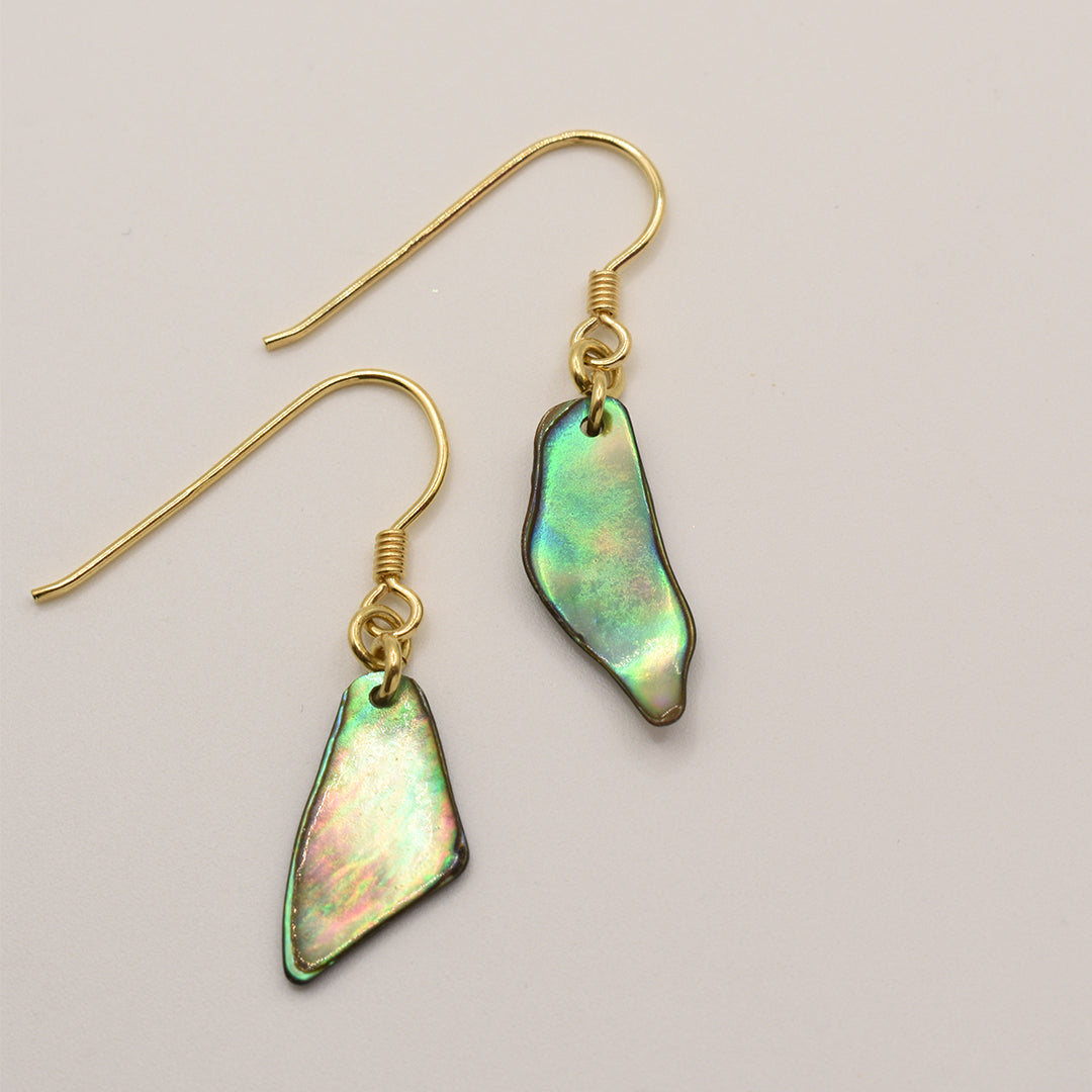 Salty Dreamers’ Paua Shell Uru earrings feature gold hooks and iridescent, irregular pāua shell pendants—New Zealand sea opal—shown on a light beige background.
