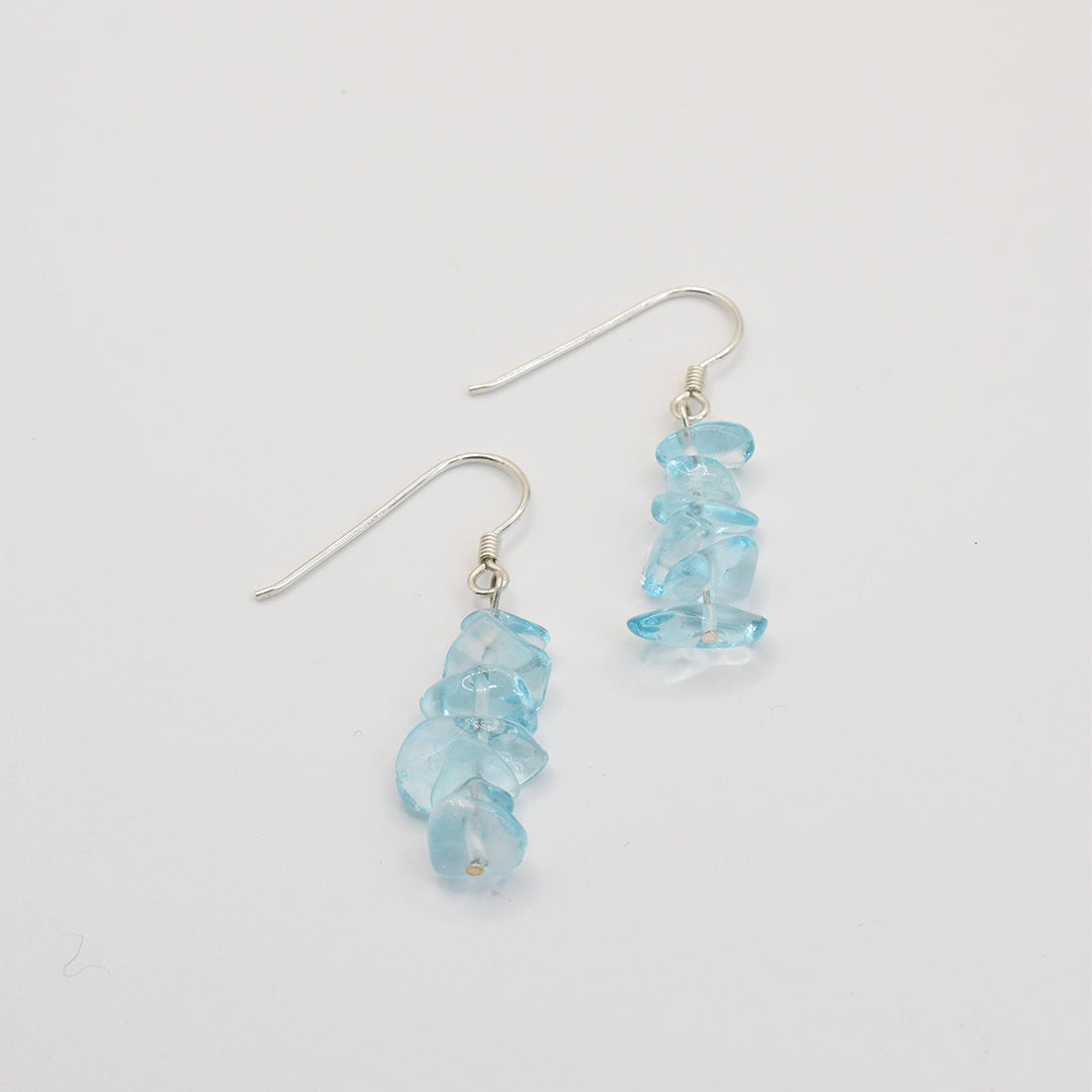 The Glassy Spring earrings by Salty Dreamers feature clusters of irregular, translucent blue glass stones and 925 silver hooks, displayed vertically on a plain white background.