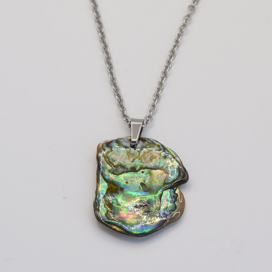 The Salty Dreamers Necklace | Paua Shell Kaukau features a handmade silver chain with an irregular paua shell pendant, showcasing shimmering green, blue, and gold hues against a white background.