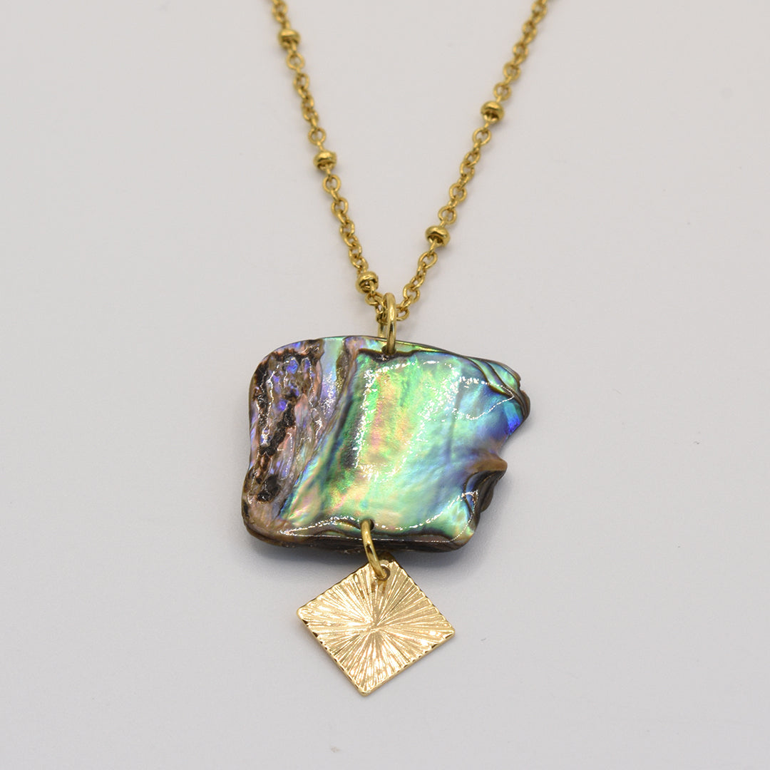 The Salty Dreamers Necklace | Paua Shell Rangi features a large, iridescent New Zealand pāua shell pendant with a small gold diamond charm on a gold chain, shown against a plain light background.