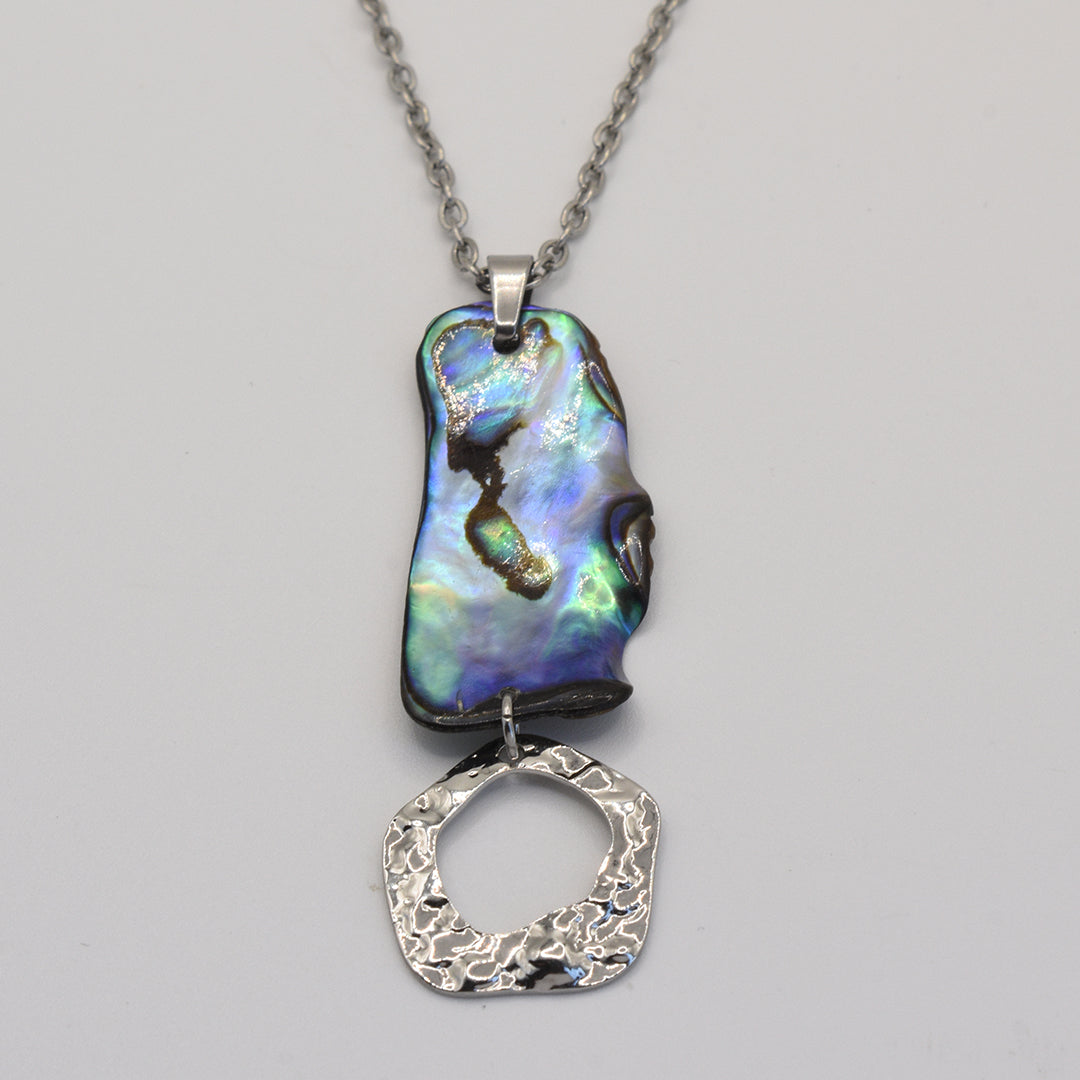 The Salty Dreamers Necklace | Paua Shell Atea showcases an iridescent, irregular paua shell above a textured silver-toned ring on a metal chain, presented against a plain background.