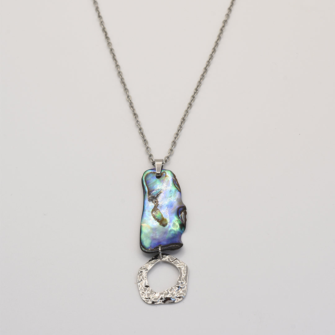 The Necklace | Paua Shell Atea by Salty Dreamers showcases a handmade silver chain with an iridescent, irregular paua shell pendant and a textured silver ring, displayed on a plain light background.