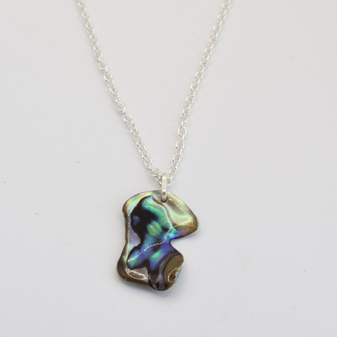 The Salty Dreamers Necklace | Paua Shell Kea features a handmade silver pendant with an irregular pāua shell, showcasing shimmering green, blue, and purple hues on white.