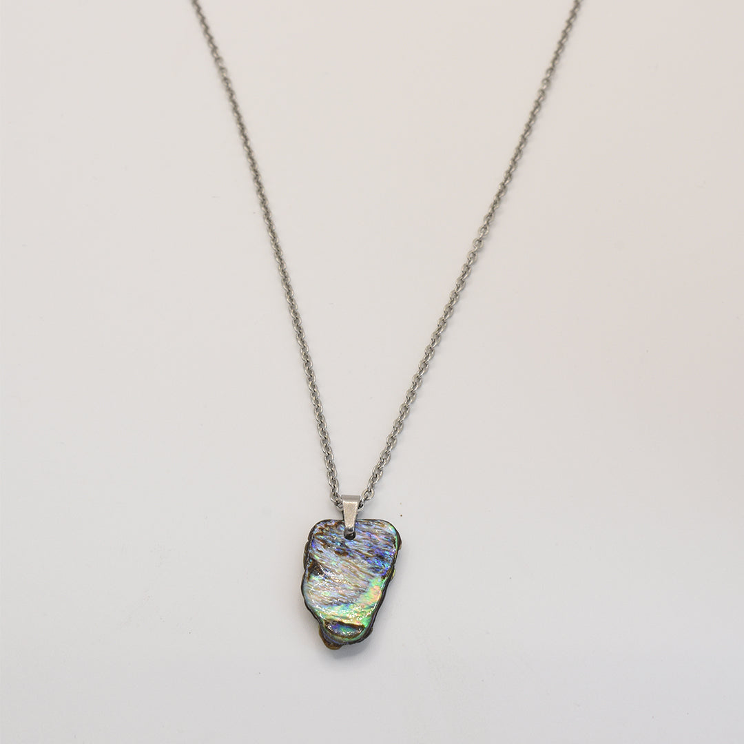 The Necklace | Paua Shell Pae by Salty Dreamers features an iridescent, irregular paua shell pendant in blue, green, and gold on a silver chain, beautifully presented on a white background—a stunning example of handmade New Zealand jewelry.