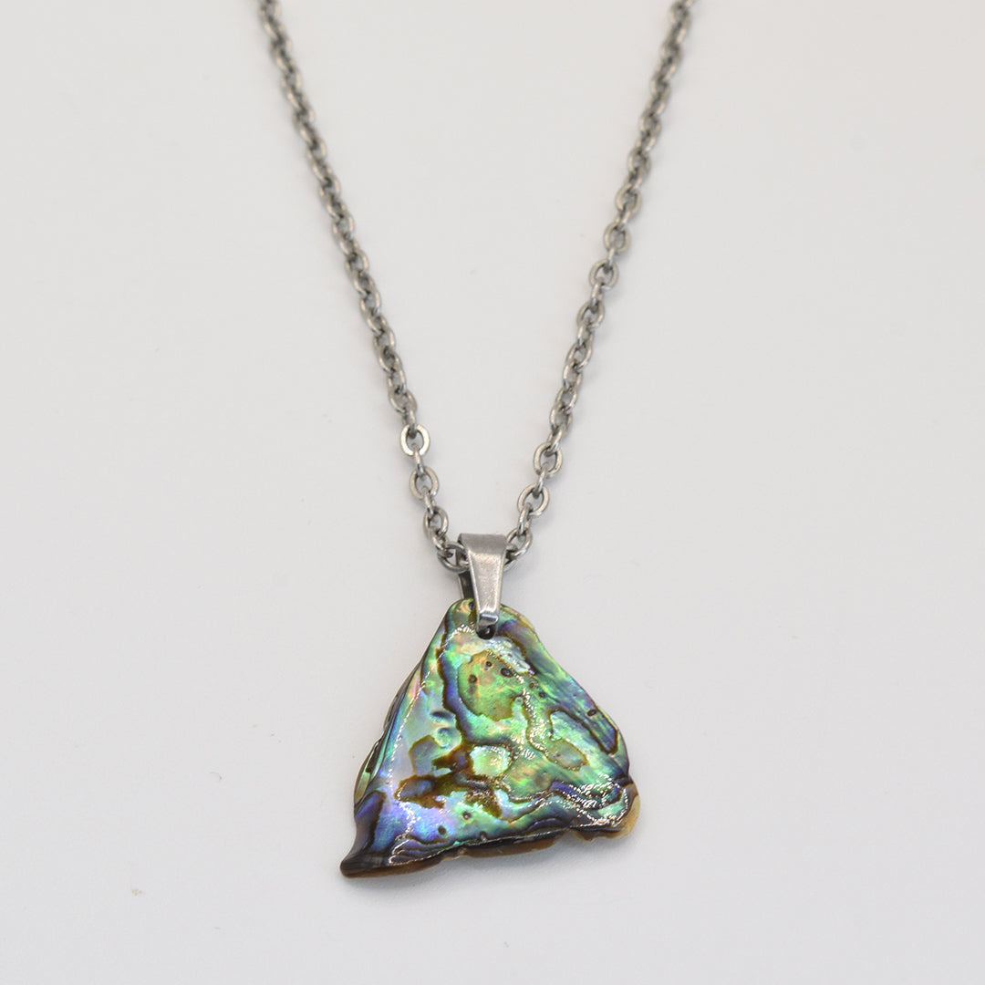 The Salty Dreamers Paua Shell Ngaru necklace features a handmade silver chain and a triangular, iridescent abalone pendant with green, blue, and gold hues, shown on a white background.