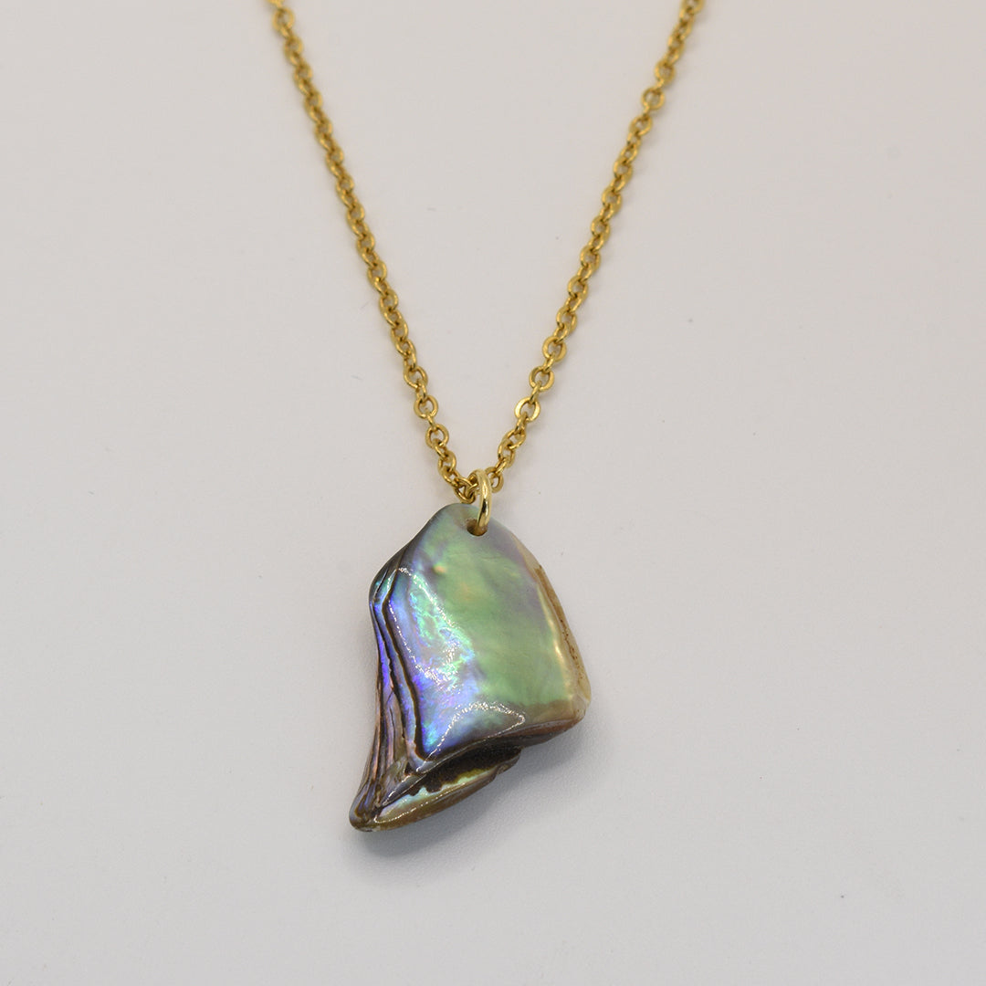The Salty Dreamers Necklace | Paua Shell Aroha features an iridescent, irregularly shaped golden pāua shell pendant on a gold chain—a stunning piece of New Zealand jewelry set against a plain white background.