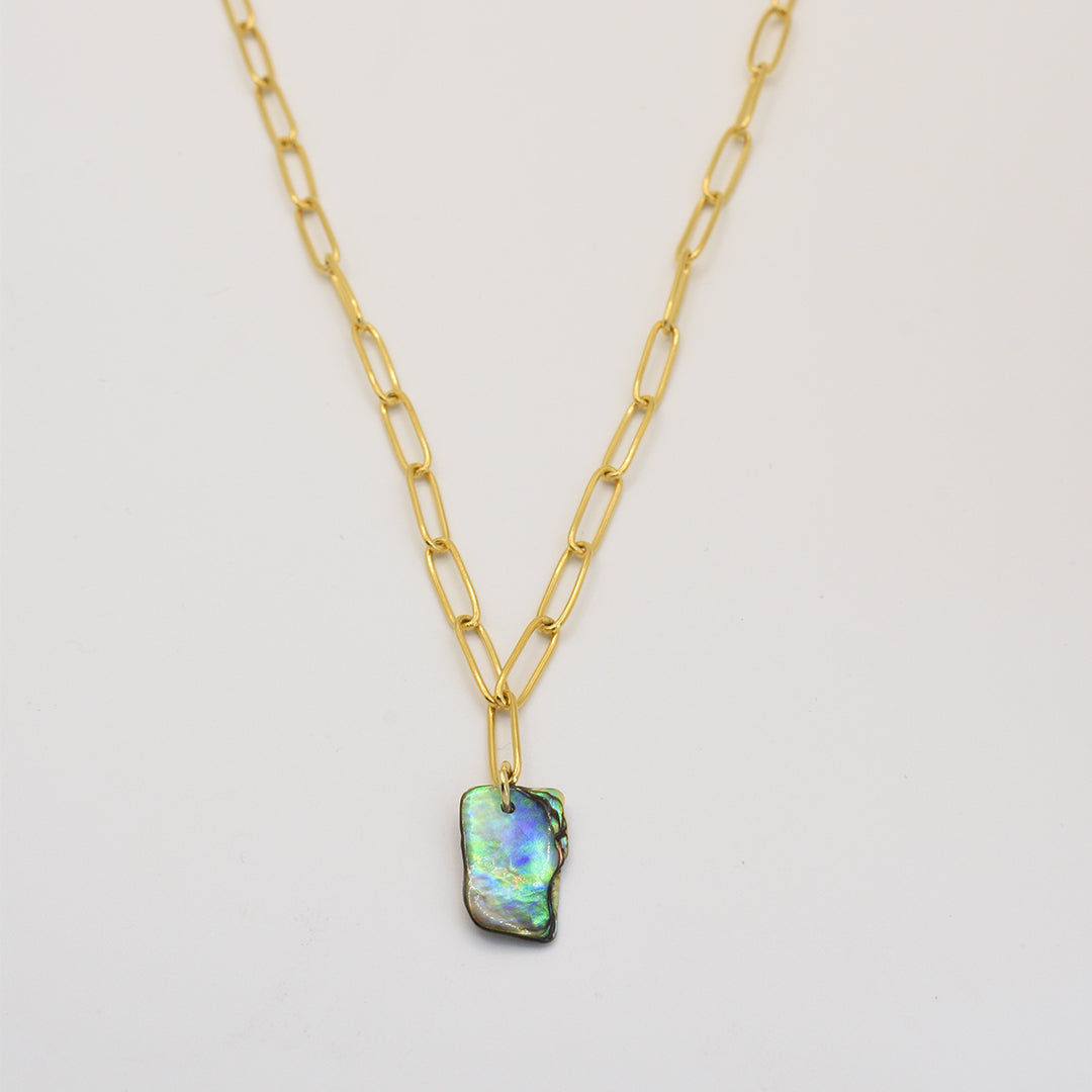 The Paua Shell Tautahi Necklace by Salty Dreamers features a gold paperclip chain and a rectangular iridescent abalone pendant, highlighting handmade beauty against a white background.