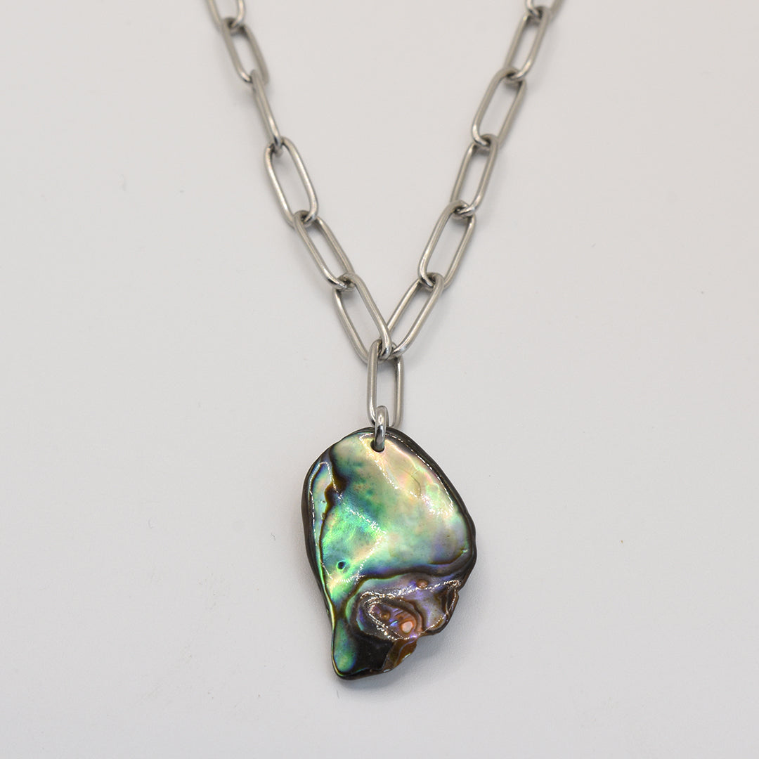 The Salty Dreamers Necklace | Paua Shell Tu is a silver stainless steel necklace with a large, uniquely shaped paua shell pendant in green, blue, and purple iridescence, displayed against a plain white background.