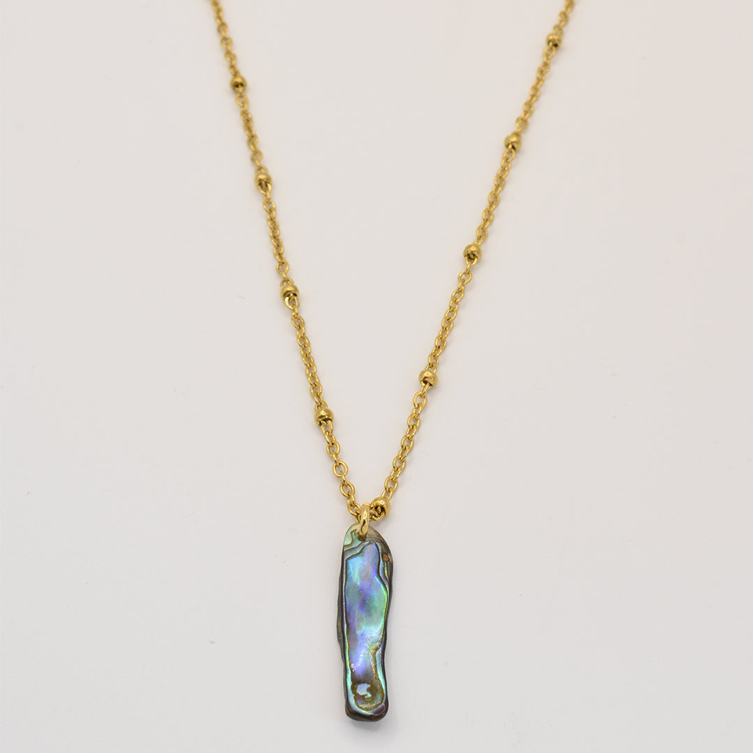Salty Dreamers Paua Shell Ra Necklace—a gold chain with small beads and a vertical iridescent paua shell pendant, handmade and inspired by New Zealand jewelry, shown on a plain white background.