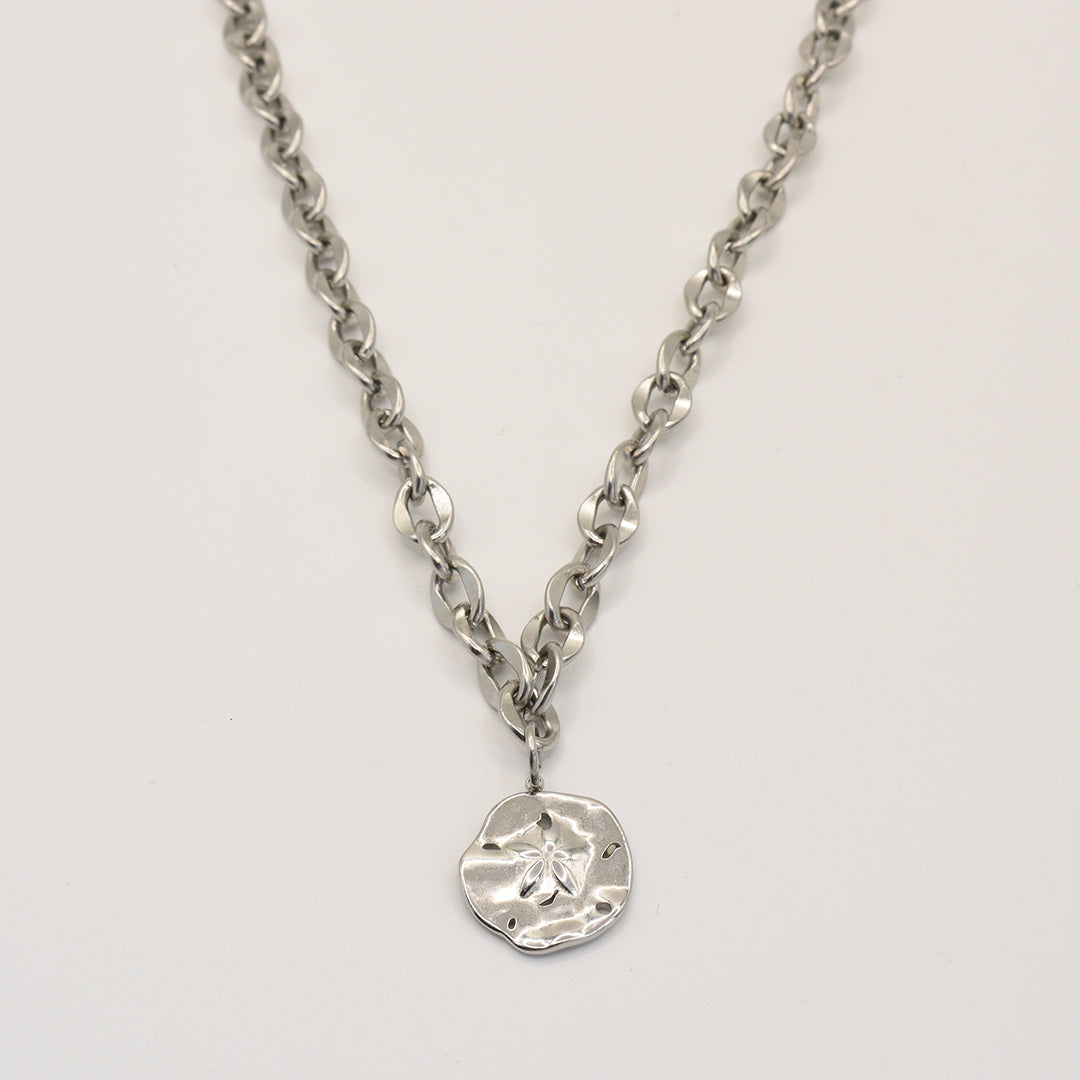 The Necklace | Ocean Dollar Silver by Salty Dreamers features large, round silver links and a textured sand dollar pendant, crafted from stainless steel and showcased against a plain white background.