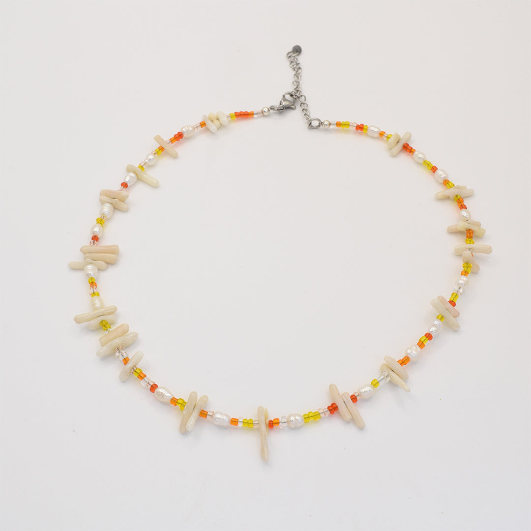 The Salty Dreamers Necklace | Ocean Bamboo Orange features small orange, yellow, and white beads with irregular ivory pieces and a silver adjustable clasp, arranged in a circle on a white background.