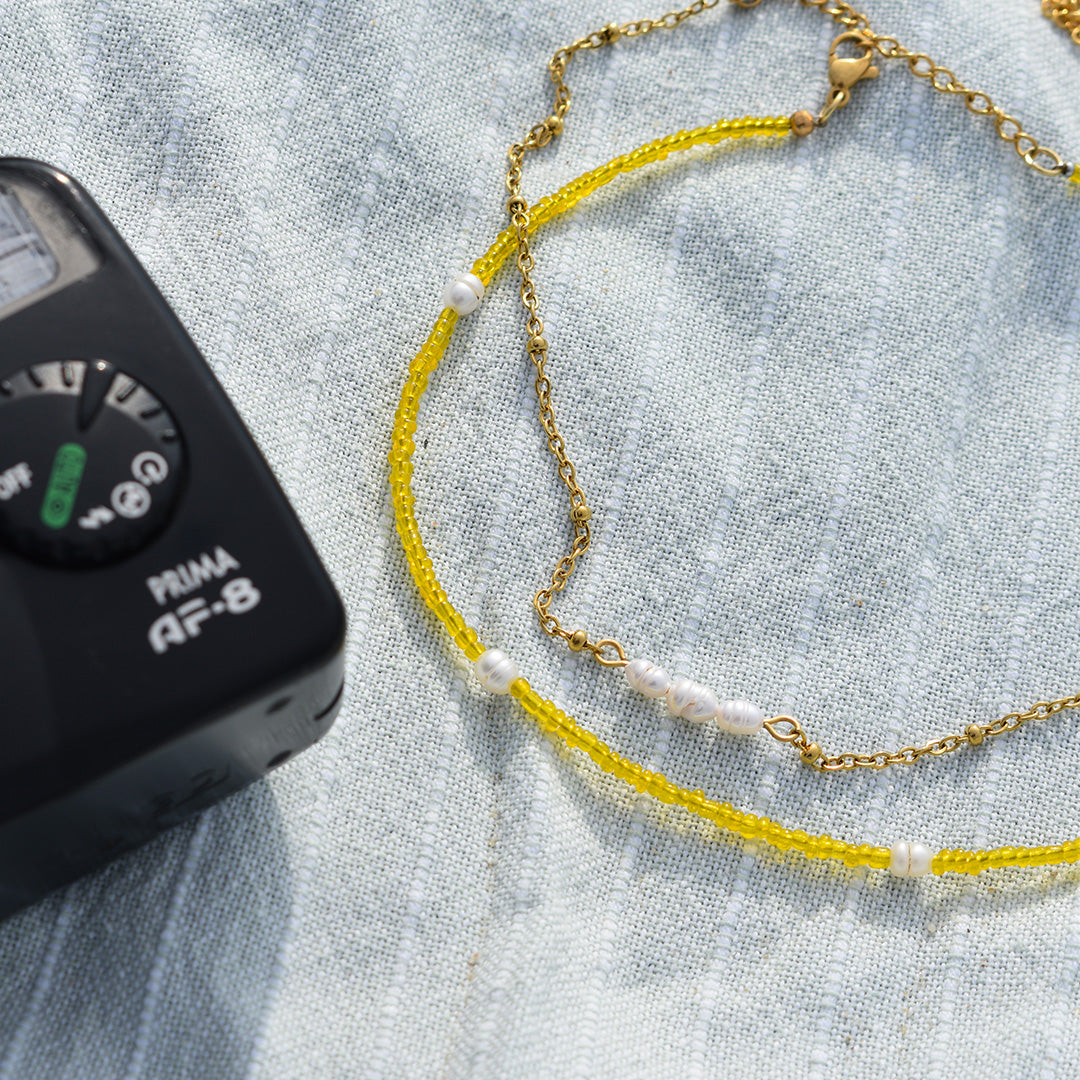 The Salty Dreamers Necklace | Starfish, featuring colorful handmade beads and small pearls, is displayed on light blue textured fabric beside the corner of a black electronic device.