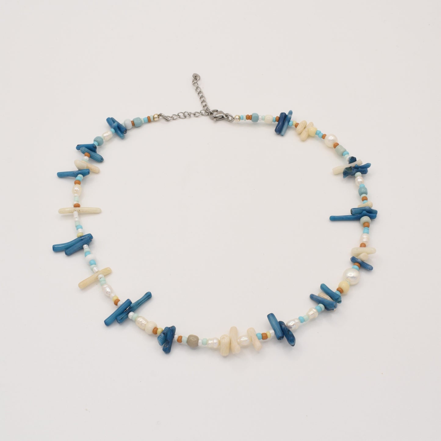 The Salty Dreamers Necklace | Ocean Bamboo Blue is a handmade piece with irregular blue and cream stick beads, turquoise and brown rounds, and white pearls, finished with a silver adjustable clasp. Displayed on a white background.