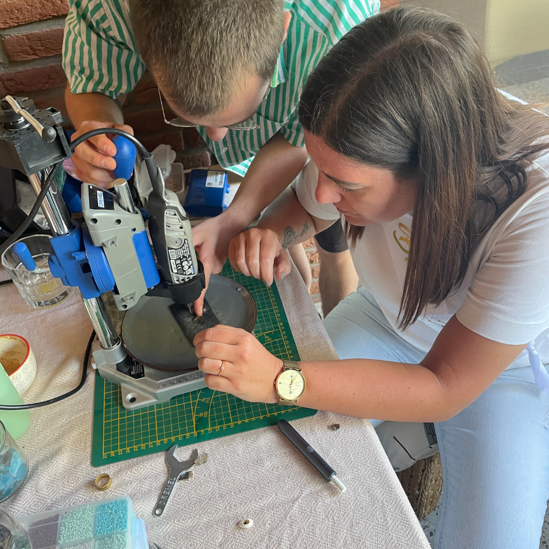 Two people working on a workshop project involving a power tool on a table drilling a shell.