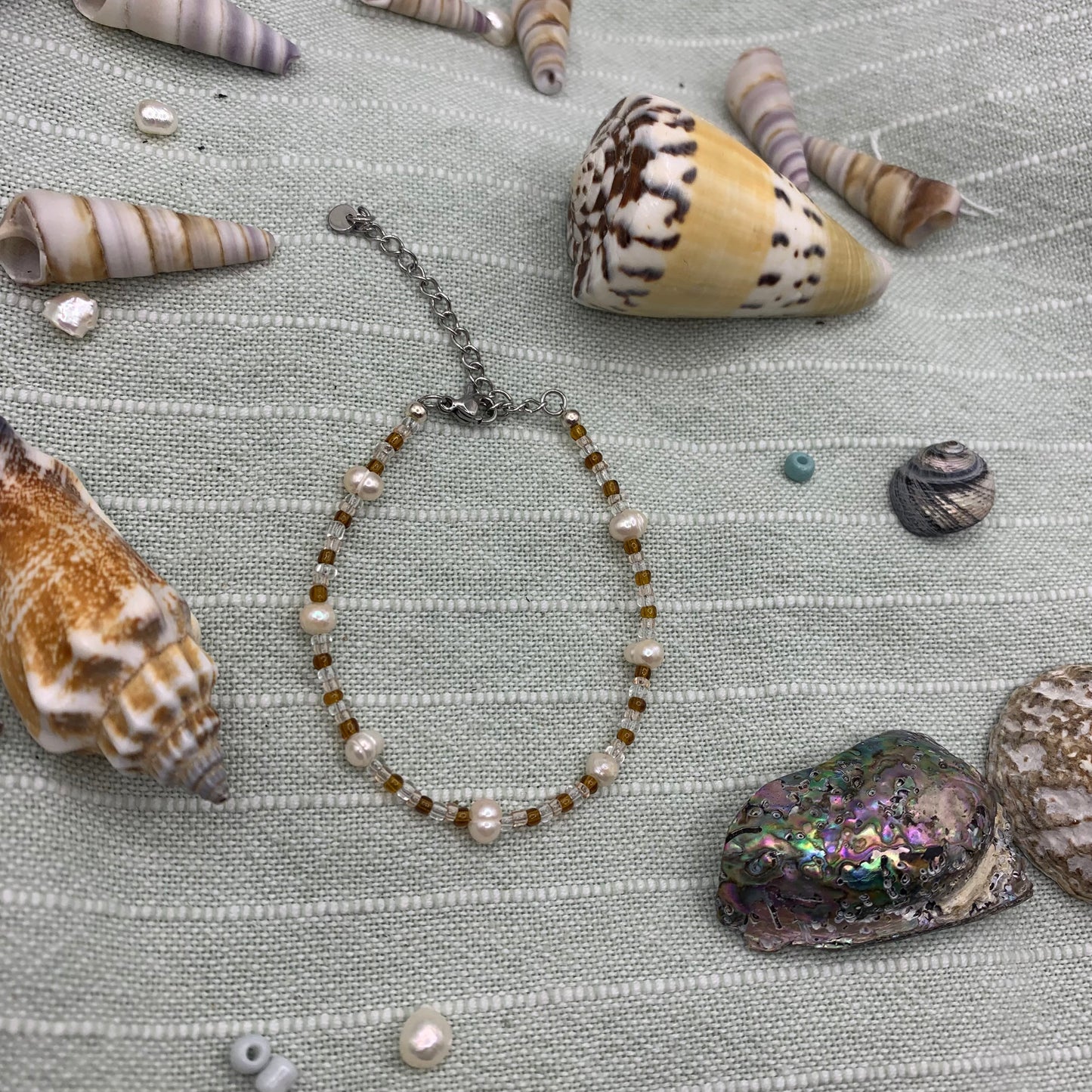 Necklace with pearls and beads surrounded by seashells on a textured fabric background