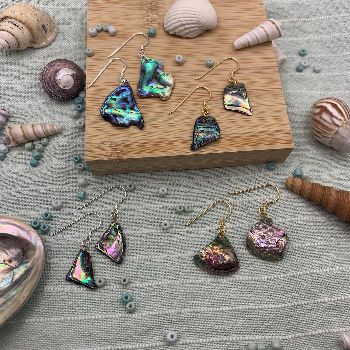 Salty Dreamers’ Earrings | Paua Shell Surprise Pieces feature iridescent paua shell on gold and 925 silver hooks, displayed with shells and blue beads. Each handmade pair includes a jewellery bag.