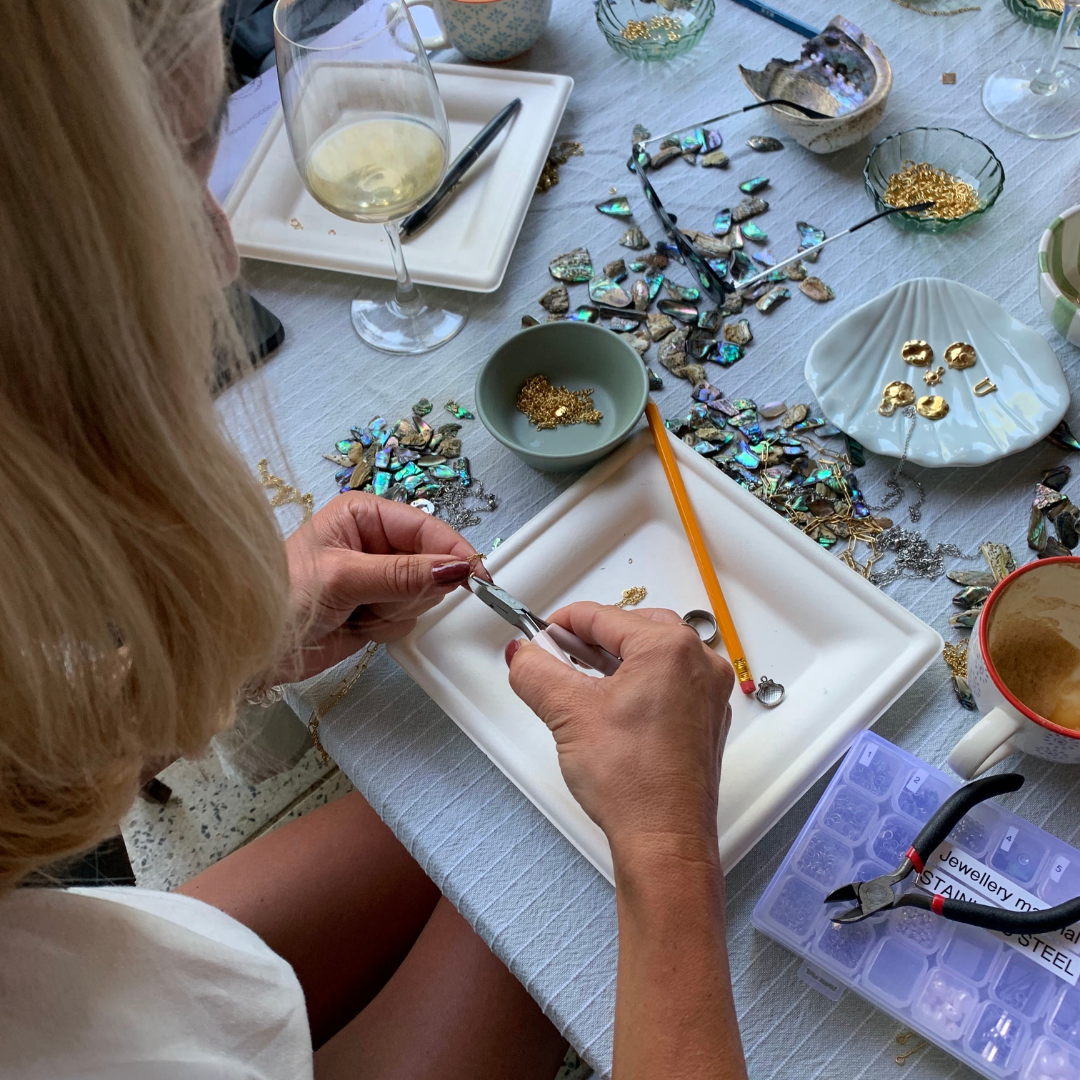 Person working on jewelry at a table with various materials and tools.