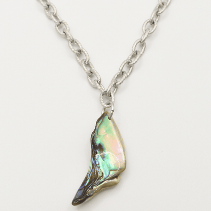 The Salty Dreamers Necklace | Paua Shell Hau features a handmade silver chain with a wing-shaped pendant, crafted from iridescent pāua shell in green, pink, and blue tones on a white background.
