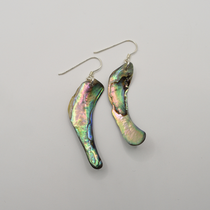 Salty Dreamers' Earrings | Paua Shell Toa feature asymmetrical, iridescent pāua shells with silver hooks. Displayed on a white background, these handmade earrings highlight natural beauty in a unique style.