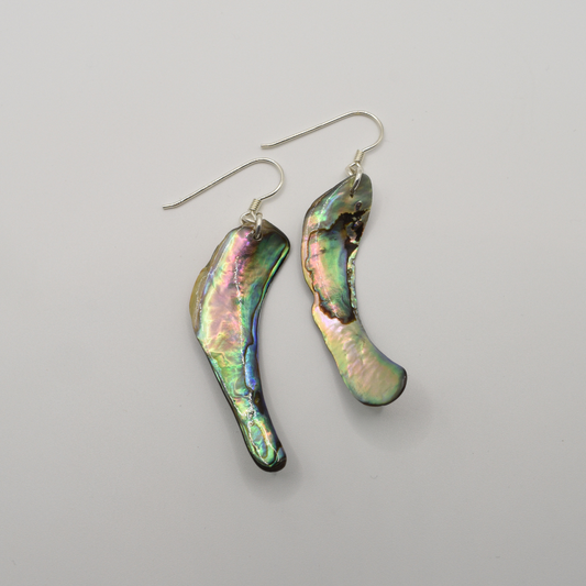 Salty Dreamers' Earrings | Paua Shell Toa feature asymmetrical, iridescent pāua shells with silver hooks. Displayed on a white background, these handmade earrings highlight natural beauty in a unique style.